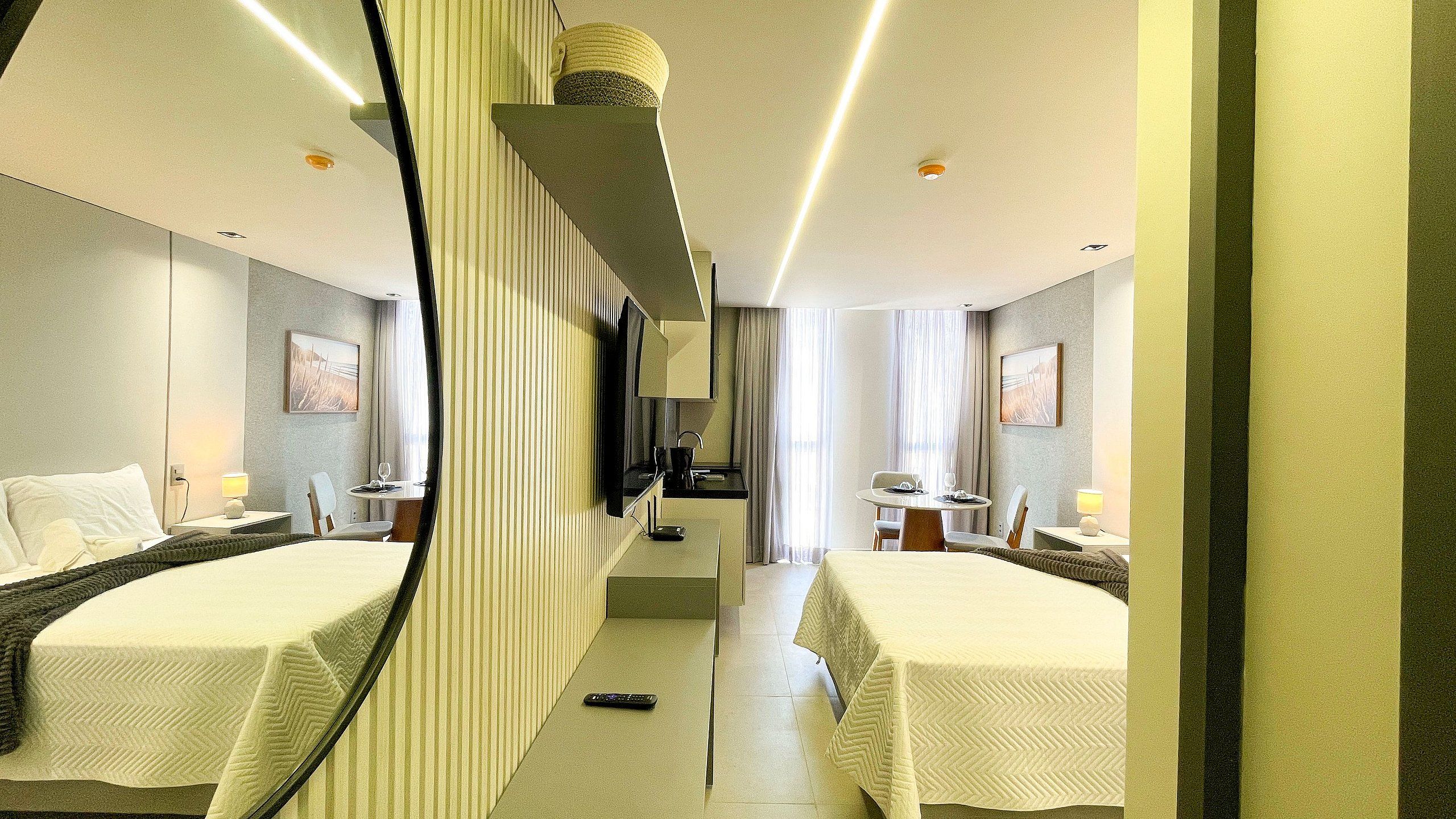 A hotel room with two beds, a small kitchenette, a sitting area with a table and chairs, and a large mirror.