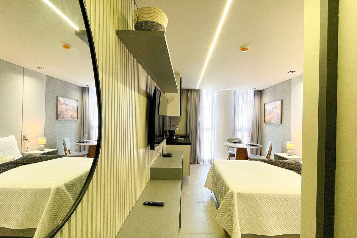 A hotel room with two beds, a small kitchenette, a sitting area with a table and chairs, and a large mirror.