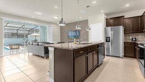 A modern kitchen with a central island, stainless steel appliances, and a dining area with a view to a pool. - Last Minute Disney Getaway! Private Pool & Themed Bedrooms. Book Now! #173071 (Orlando)