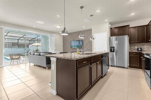 A modern kitchen with a central island, stainless steel appliances, and a dining area with a view to a pool. - Last Minute Disney Getaway! Private Pool & Themed Bedrooms. Book Now! #173071 (Orlando)