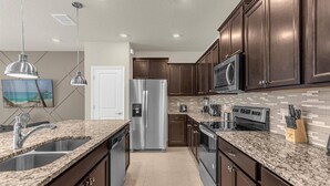 A modern kitchen with granite countertops, stainless steel appliances, and dark wood cabinets. - Last Minute Disney Getaway! Private Pool & Themed Bedrooms. Book Now! #173071 (Orlando)