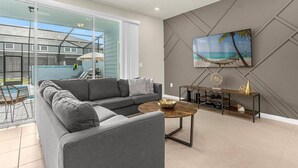 A modern living room with a grey sectional sofa, a wooden coffee table, and a flat-screen TV mounted on the wall. - Last Minute Disney Getaway! Private Pool & Themed Bedrooms. Book Now! #173071 (Orlando)