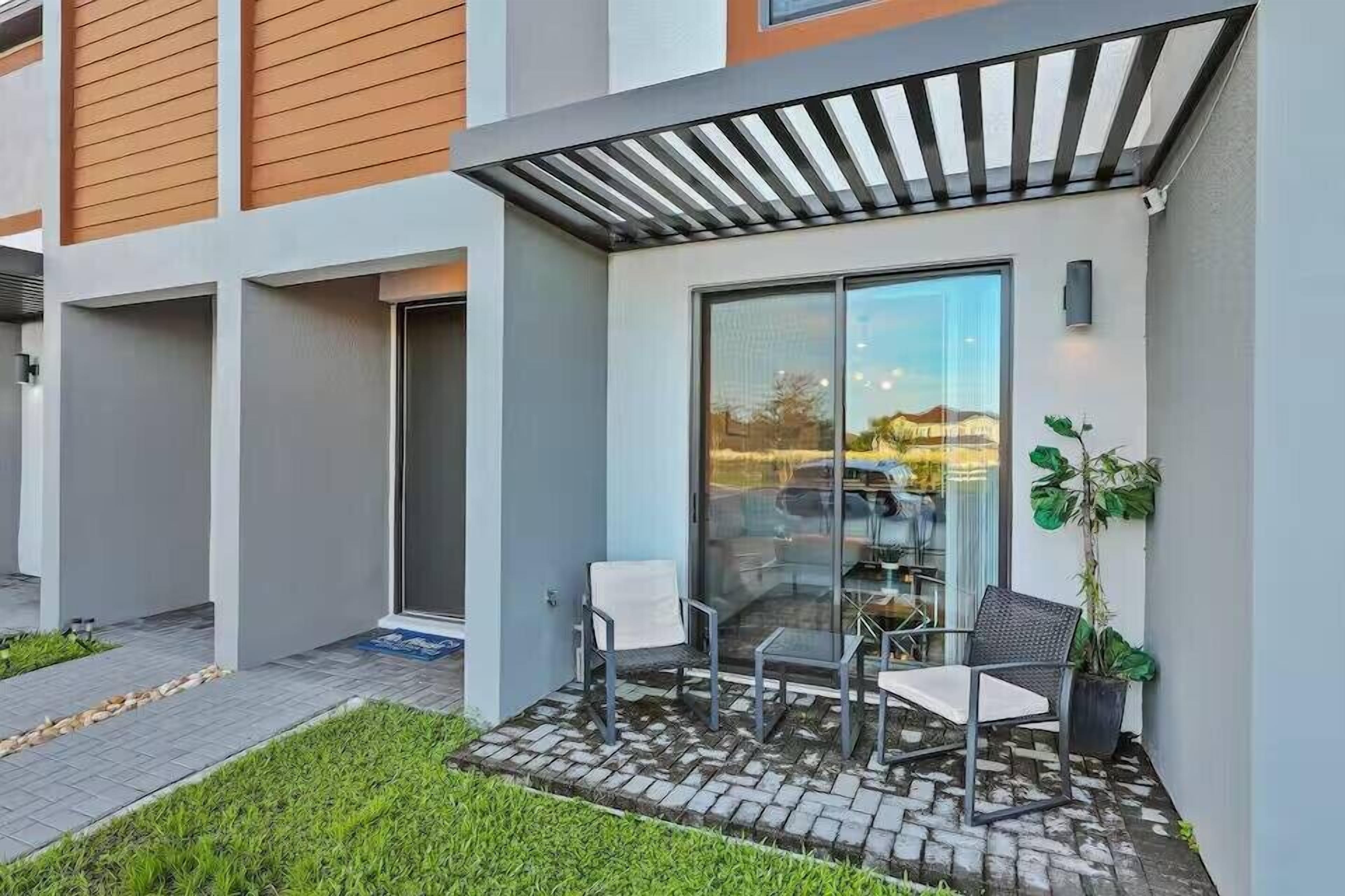A modern building with a glass door entrance, outdoor seating, and a small garden area.