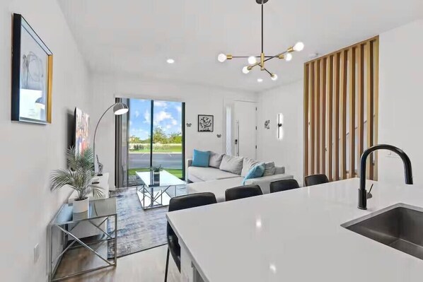 A modern kitchen with a large island, a dining area with a glass table, and a living room with a sofa and a view of the outdoors. - Last Minute Disney Getaway! Bright and Modern Townhouse with Terrace. Book Now! #172835 (Orlando)