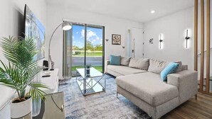 A modern living room with a sofa, a coffee table, a TV, and a large window with a view of the outdoors. - Last Minute Disney Getaway! Bright and Modern Townhouse with Terrace. Book Now! #172835 (Orlando)