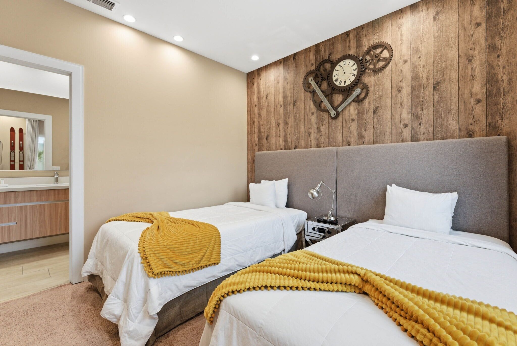 A hotel room with two beds, a wooden wall clock, a mirror, and a wooden dresser.