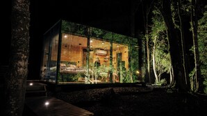 Una casa moderna de vidrio con terraza de madera, rodeada de árboles.