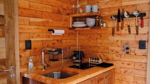 Cocina tipo cabaña de madera con un lavamanos empotrado, un aire acondicionado blanco y paredes de madera.
