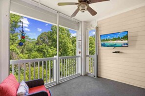 Ein Balkon mit Deckenventilator, Fernseher und Blick auf eine tropische Landschaft.