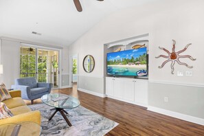 Ein geräumiges Wohnzimmer mit großem Fernseher, bequemen Sitzmöglichkeiten und Blick ins Freie.