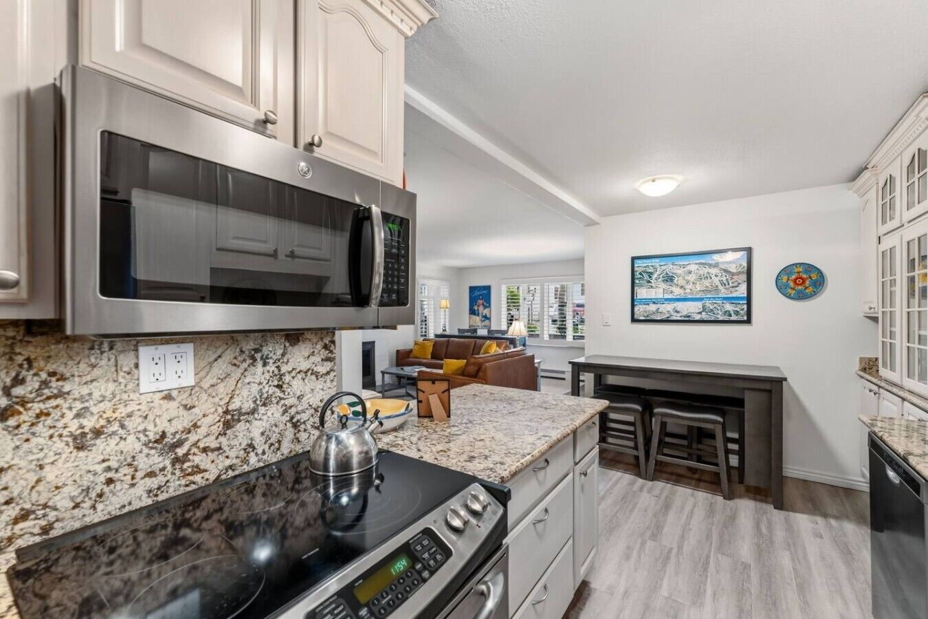 A modern kitchen with a built-in microwave, stove, and granite countertop. There is a dining area with a bar and a seating arrangement.