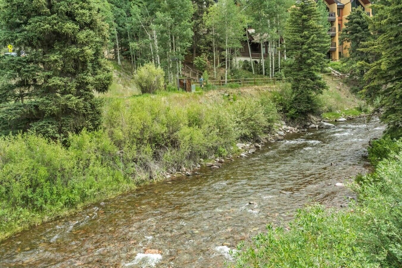Un río fluye por una zona boscosa, con un edificio al fondo.