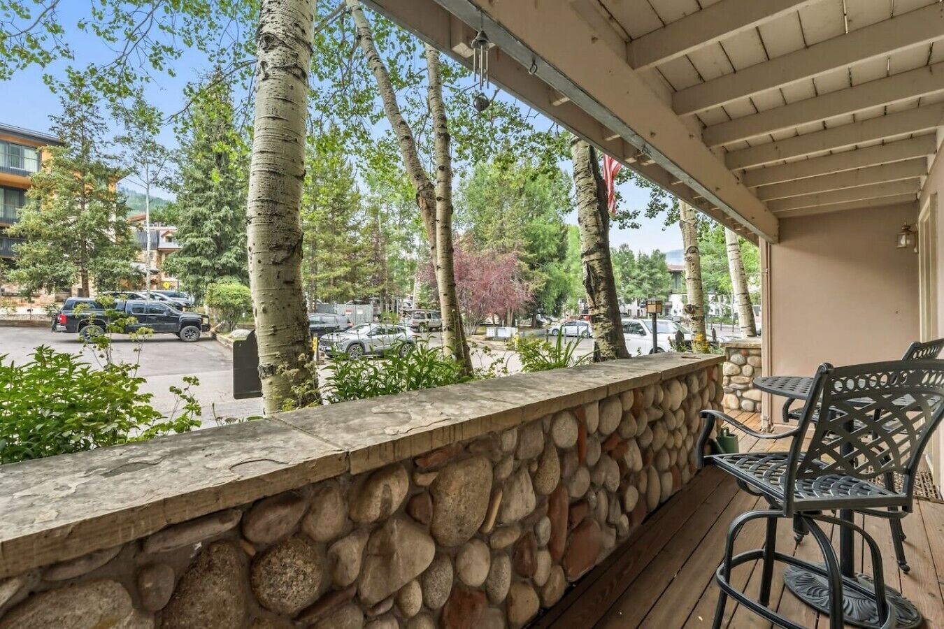 A covered outdoor area with a stone wall, wooden deck, and metal chairs.