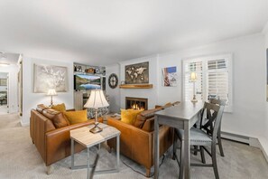 A living room with a fireplace, a television, and a dining area with a table and chairs. - Creekside Condo in Vail Village I Walk to Gondola (Vail)