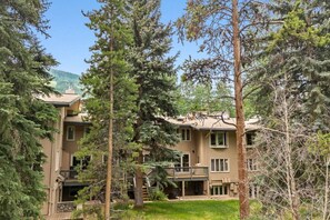 A two-story building surrounded by tall evergreen trees. - Creekside Condo in Vail Village I Walk to Gondola (Vail)