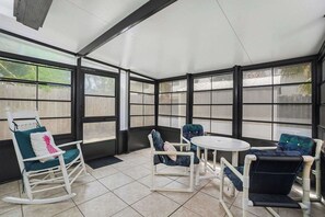 Ein überdachter Patio-Bereich mit einem Schaukelstuhl, zwei gepolsterten Stühlen und einem kleinen runden Tisch.
