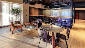 A modern lounge area with a round table, chairs, a potted plant, and a large window with curtains. - Loft Elegance 2 bed | Gym • Pet Friendly • AC (Guadalajara)