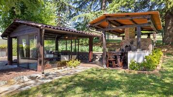 A covered outdoor seating area with a brick structure, stone pillars, and a wooden roof.