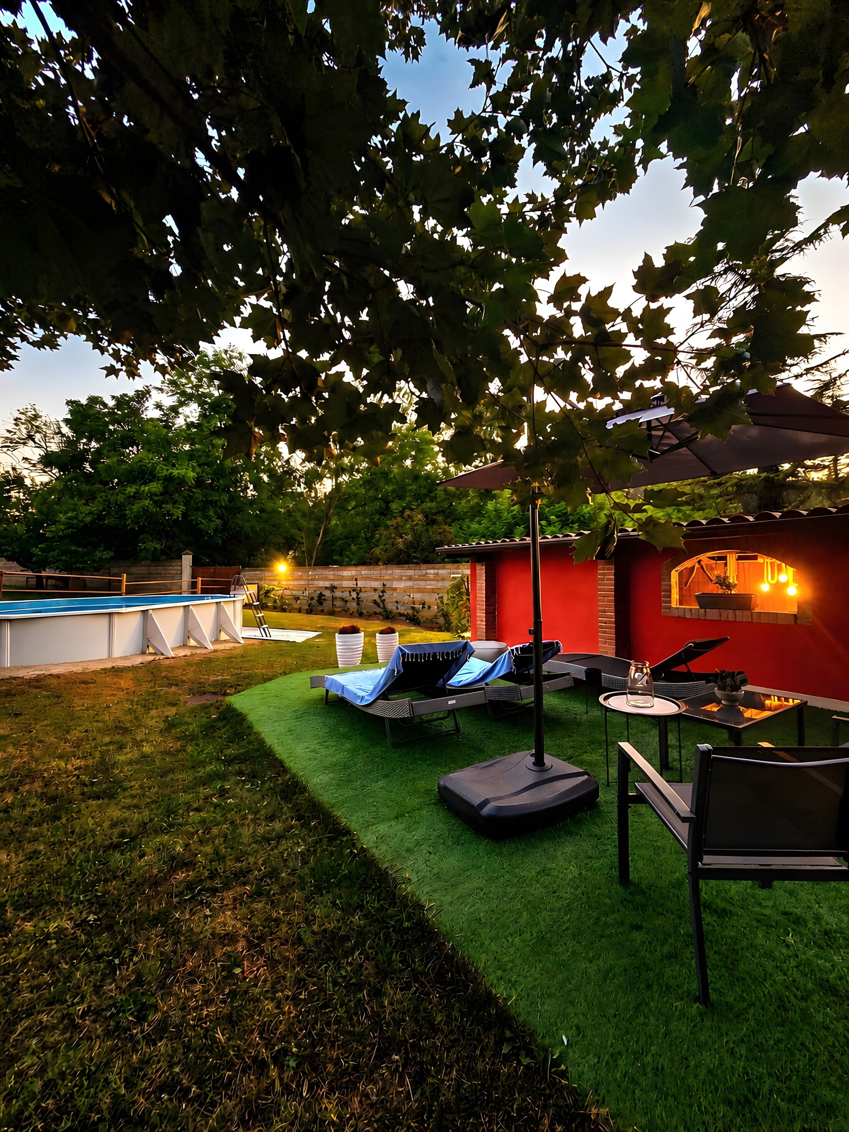 Un patio trasero con césped artificial, una piscina, sillas de descanso y una zona de barbacoa.