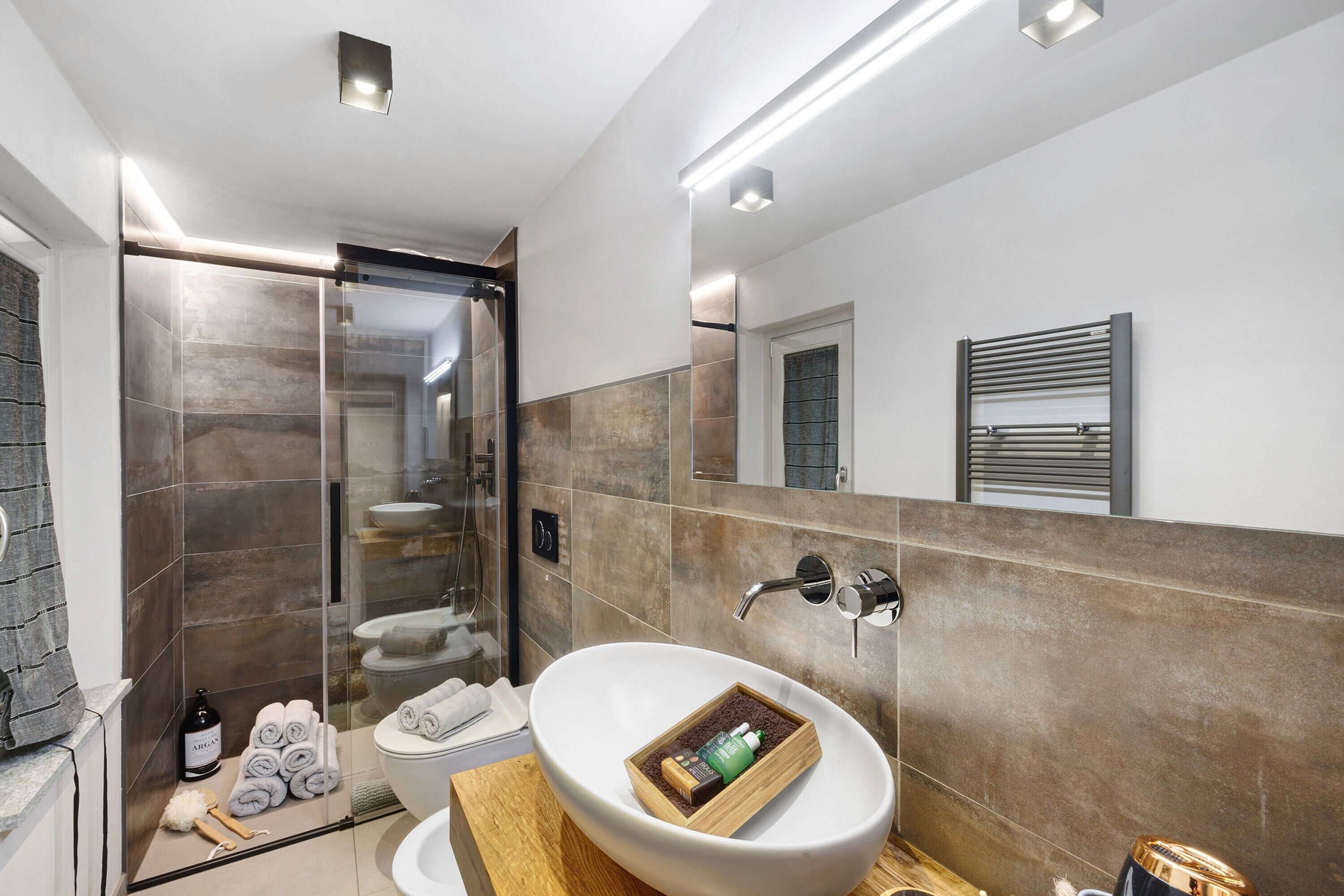 A modern bathroom with a large white sink, a glass shower enclosure, and a towel rack.