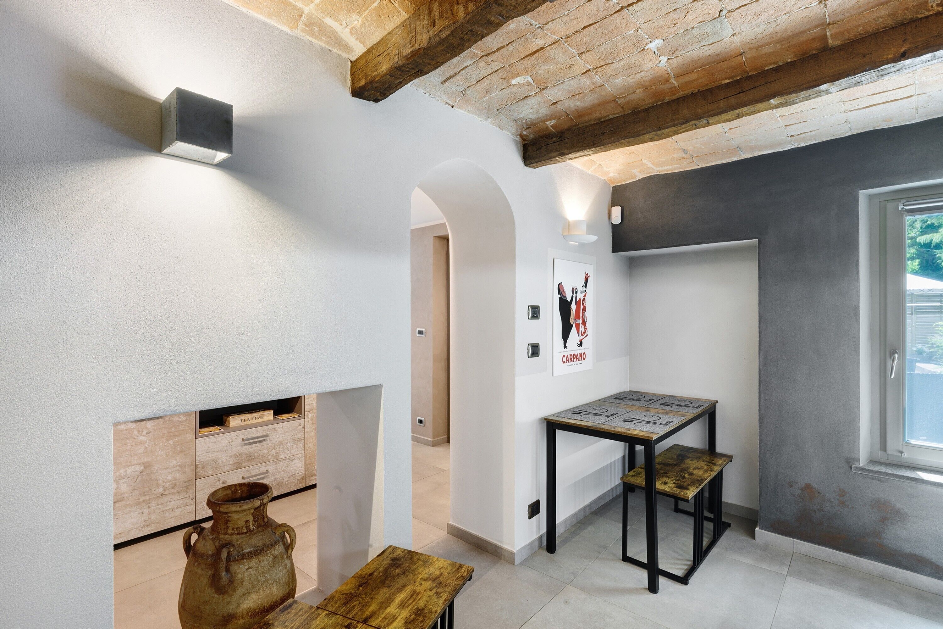 Una stanza con travi a vista in legno, un muro bianco con un quadro appeso, un tavolino con una mappa e una finestra vista panoramica.