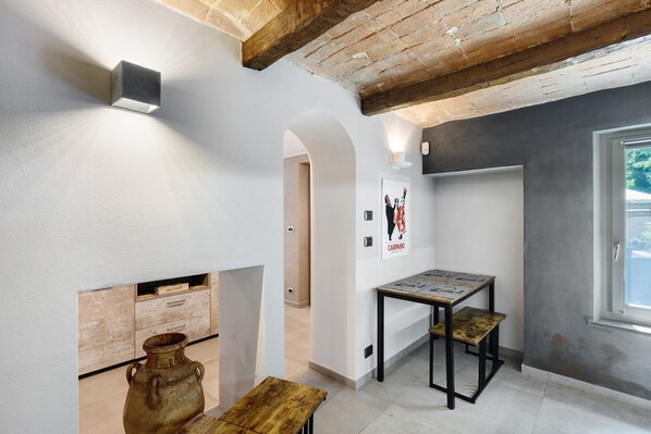 A room with exposed wooden beams, a white wall with a framed picture, a small table with a map, and a window with a view.