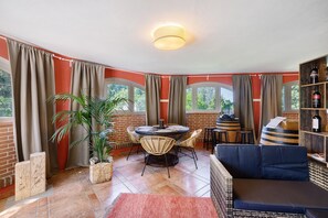 Et værelse med et rundt bord, stole, en sofa, en potteplante og et vinskab.
