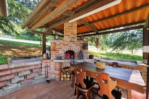 Une terrasse extérieure avec une cheminée en briques, une table en bois et des chaises.