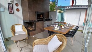 Un comedor con mobiliario de mimbre, una chimenea y vistas al exterior.