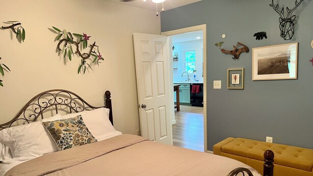 A bedroom with a bed, a bedside table, a door leading to a bathroom, and a wall-mounted shelf with decorative items. - Woodland Edge Retreat- Borders NRG National Park, trail access from backyard (Fayetteville)