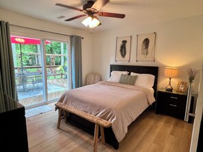 Ein Schlafzimmer mit einem Bett, einem Nachttisch, einer Lampe, einem Deckenventilator und Blick ins Freie durch eine Schiebetür.