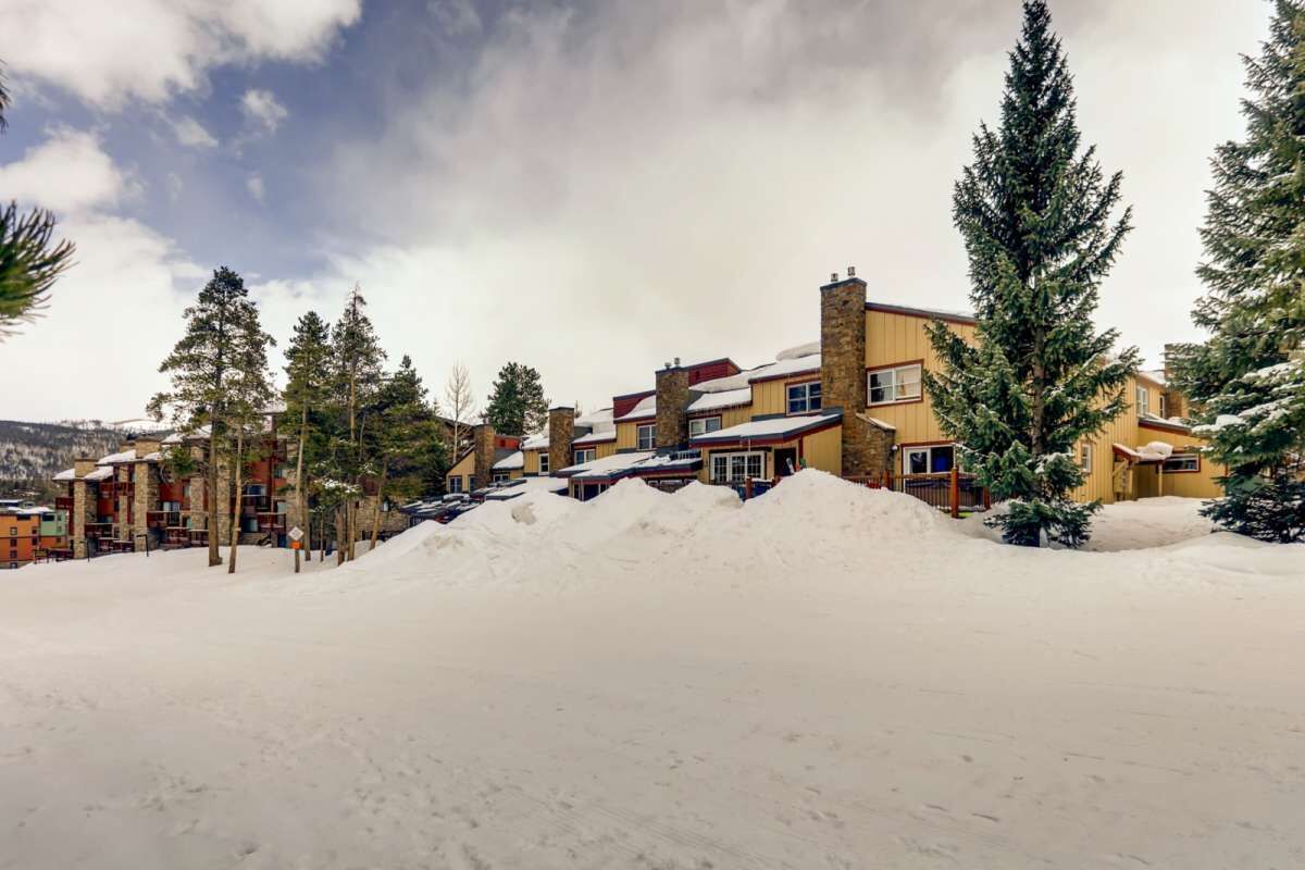Ein mit Schnee bedecktes Gebäude mit mehreren Schornsteinen, umgeben von Schnee und Bäumen.