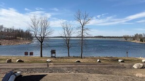 A lakeside view with a dirt path, a bench, and a signboard.