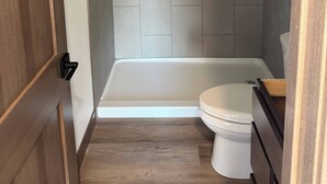 A bathroom with a bathtub, toilet, and wooden flooring.