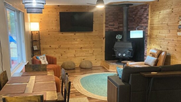 Una sala de estar acogedora con chimenea, paredes de madera, un comedor con sillas y un sofá.