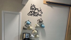 Una kitchenette con cafetera, tazas y un adhesivo en la pared que dice 'La vida comienza después del café'.