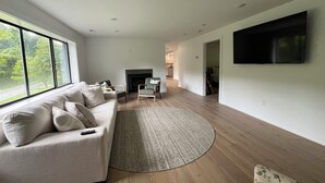 En moderne stue med sofa, lænestole, pejs, fladskærms-tv og et stort vindue.