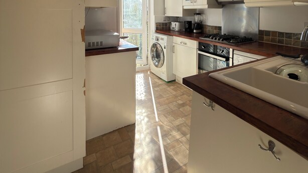 A modern kitchen with white cabinets, a microwave, a washing machine, and a sink. - Wiltern Court (London)