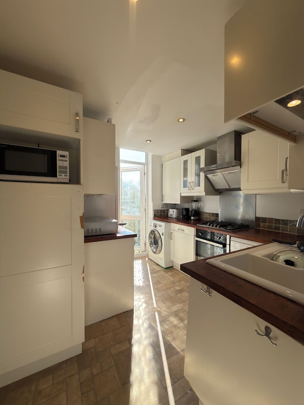 A modern kitchen with white cabinets, a microwave, a washing machine, and a sink.