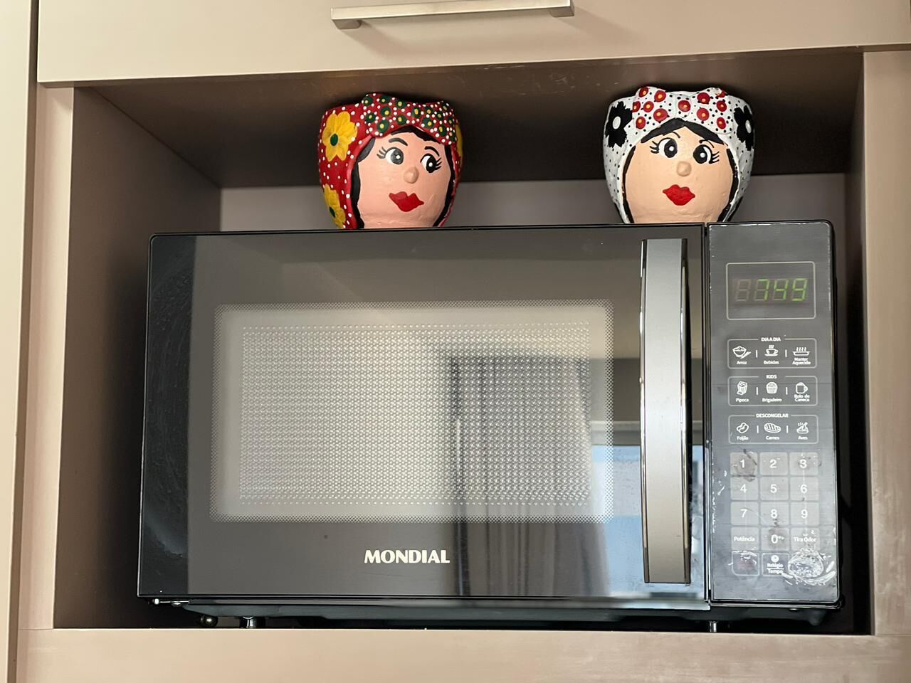 Een magnetron in een keukenkastje, met twee decoratieve objecten erop.