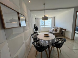 A dining area with a round table, black chairs, and a white tablecloth. - Clocio Beltrão 205 - Beachfront Apartment on Cabo Branco Beach for 4 people (João Pessoa)
