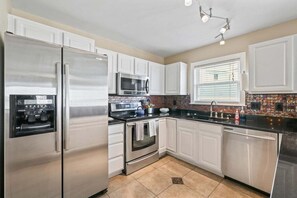 A kitchen with white cabinets, stainless steel appliances, a microwave, and a tiled backsplash.