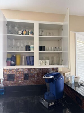 A kitchen with a coffee maker, shelves with glassware, and a tiled backsplash.
