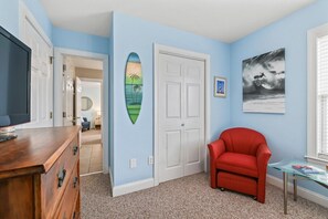 Ein Zimmer mit einem Holzkasten, einem roten Sessel, einem Glastisch, einer weißen Tür und zwei gerahmten Bildern an der Wand.