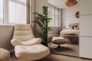 A room with a large mirror, a beige armchair, a potted plant, a bed with a woven blanket, and a hanging light fixture. - Nearmere, Slps 8, Central, Parking, Balcony, Views (Bowness-on-Windermere)