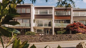 Un immeuble résidentiel moderne à plusieurs étages, avec un mur en pierre à l’avant, des balcons et un ciel dégagé.