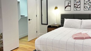 A bedroom with a bed, bedside table, lamp, and wall art. - Flamingo Grove, Vibrant Downtown Studio Escape, AC (Halifax)