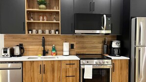 A modern kitchen with wooden cabinets, a stainless steel refrigerator, a microwave, a stove, and a sink. - Flamingo Grove, Vibrant Downtown Studio Escape, AC (Halifax)