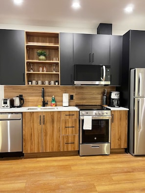 A modern kitchen with wooden cabinets, a stainless steel refrigerator, a microwave, a stove, and a sink. - Flamingo Grove, Vibrant Downtown Studio Escape, AC (Halifax)