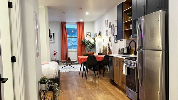 A modern kitchen with wooden flooring, stainless steel appliances, and a dining area with a red tablecloth. - Flamingo Grove, Vibrant Downtown Studio Escape, AC (Halifax)